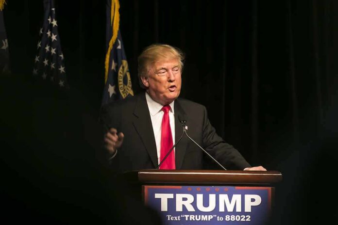 Man speaking at podium with "TRUMP" sign.
