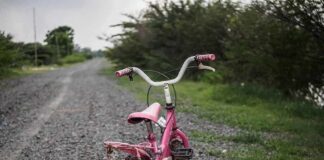 Pink children's bike with training wheels on gravel path.