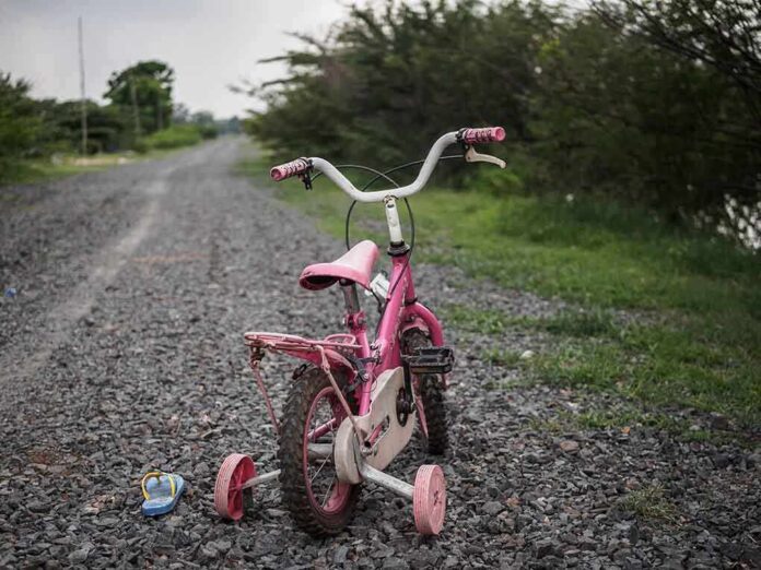Pink children's bike with training wheels on gravel path.