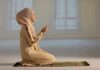 Woman praying indoors on a prayer mat.