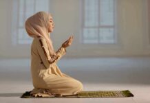 Woman praying indoors on a prayer mat.