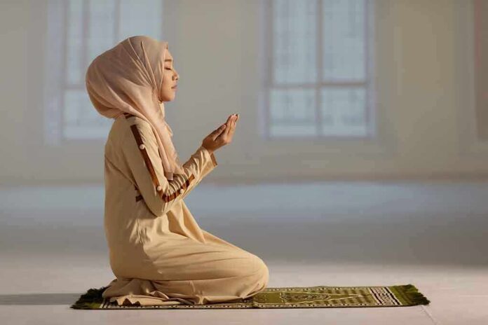 Woman praying indoors on a prayer mat.
