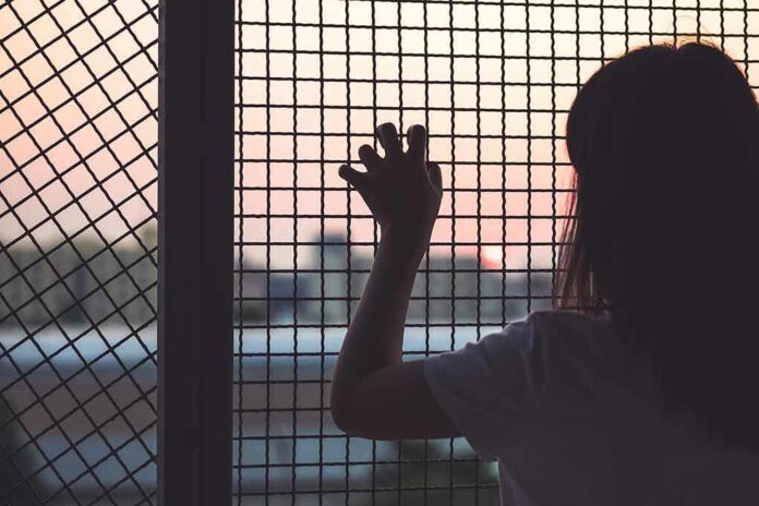 person gripping metal mesh looking out over a sunset