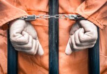 Hands cuffed behind bars in prison uniform