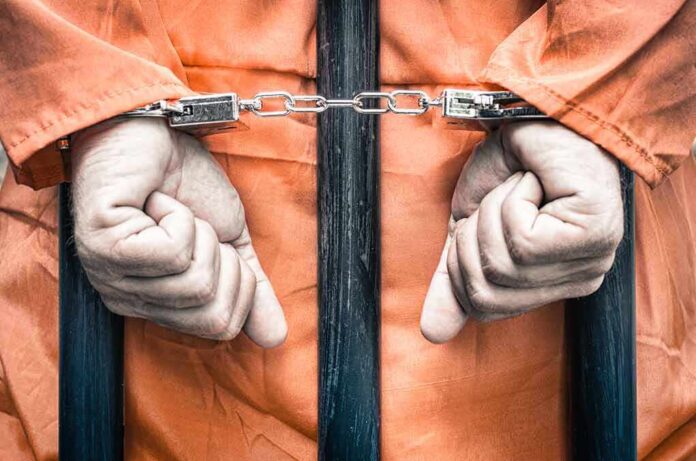Hands cuffed behind bars in prison uniform
