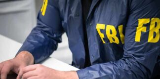 Person in FBI jacket typing on a laptop.
