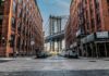 Street view with bridge between two brick buildings.