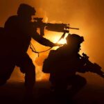 Two soldiers with weapons silhouetted against fiery background
