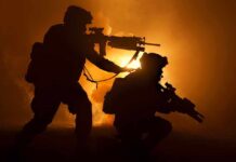 Two soldiers with weapons silhouetted against fiery background