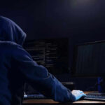 Hooded figure using dual monitors in dark room