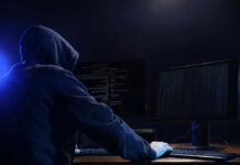 Hooded figure using dual monitors in dark room