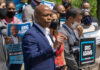 Man speaking at campaign event with supporters behind him