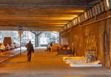 People walk under a bridge with homeless encampment