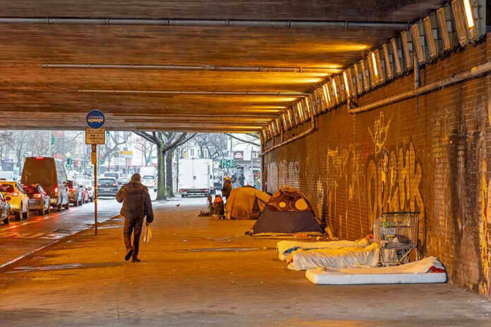 People walk under a bridge with homeless encampment