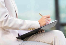Person in beige suit writing on a clipboard