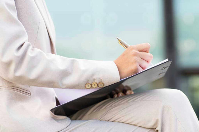 Person in beige suit writing on a clipboard