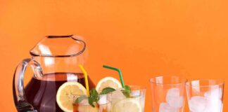 A pitcher of iced tea with lemon slices and mint, alongside glasses with ice and colorful straws
