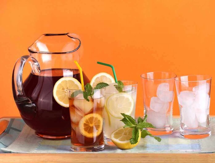 A pitcher of iced tea with lemon slices and mint, alongside glasses with ice and colorful straws