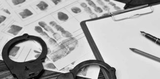 Handcuffs, fingerprint sheets, and clipboard on a desk.