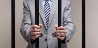 Businessman in a suit holding prison bars with handcuffs on his wrists