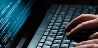 Close-up of hands typing on a laptop keyboard with code displayed on the screen