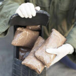 Person handling packages wearing gloves and green jacket.