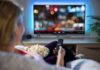 Person sitting on a couch watching a movie on a TV with popcorn in hand