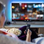 Person sitting on a couch watching a movie on a TV with popcorn in hand