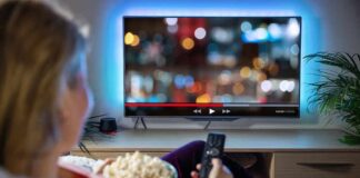 Person sitting on a couch watching a movie on a TV with popcorn in hand