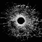 A bullet hole surrounded by shattered glass on a black background