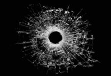 A bullet hole surrounded by shattered glass on a black background