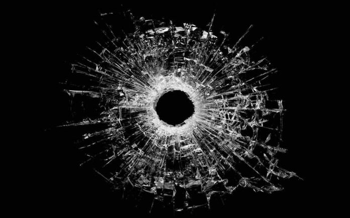 A bullet hole surrounded by shattered glass on a black background