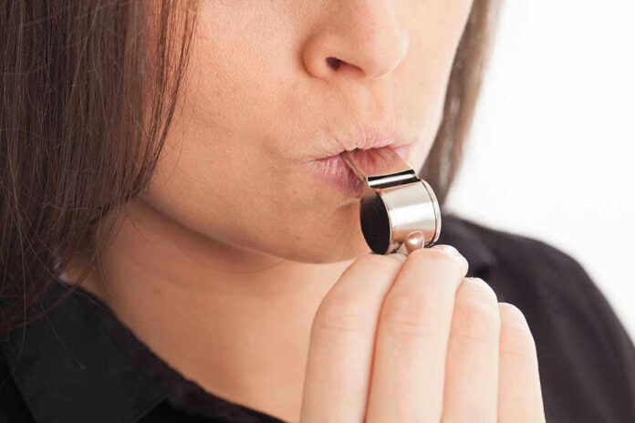 1455310238 Person blowing a silver whistle close-up.