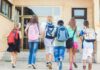 Group of children walking towards a school entrance with backpacks