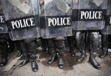 Police officers in riot gear standing behind shields marked POLICE