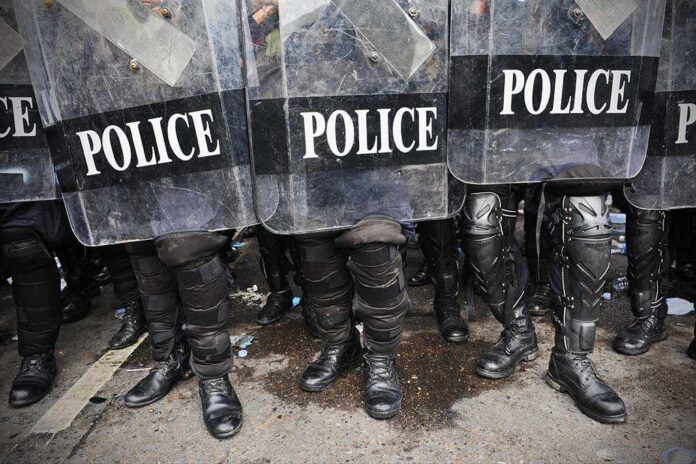 Police officers in riot gear standing behind shields marked POLICE