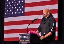 Fetterman Shocks Senate — Throws His Hat to GOP Speaker addressing an audience in front of an American flag