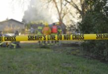 Yellow police tape marking a restricted area at a fire scene with firefighters in the background