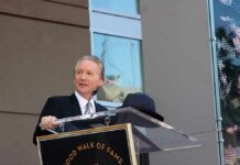 Bill Maher Sparks Chaos — Hints at Unnamed Guest A man in formal attire speaking at a podium during a Hollywood Walk of Fame ceremony
