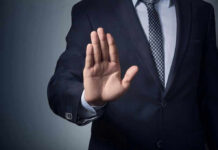 Man in suit with hand raised, signaling stop.