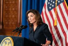 Socialist Mayor Fight EXPLODES—Hochul Cornered Kathy Hochul speaking at a podium during a press conference with an American flag in the background