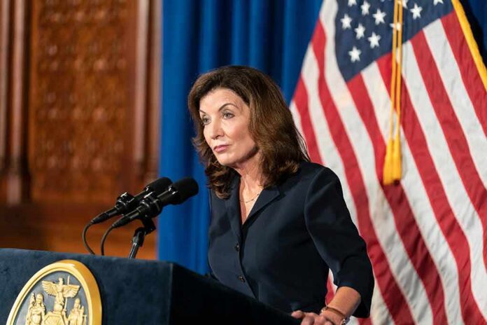 shutterstock_2023461065 (1).jpg Kathy Hochul speaking at a podium during a press conference with an American flag in the background
