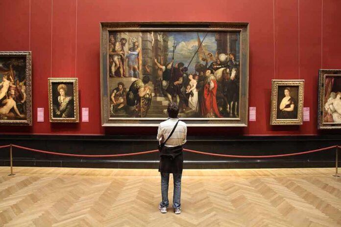 shutterstock_235506019.jpg A person standing in an art gallery, observing a large historical painting surrounded by other artworks