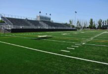 Historic Mass Suspension Rocks College Football A football field with artificial turf and empty bleachers under a clear blue sky