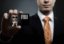 A man in a suit holding an FBI identification card while making a shushing gesture