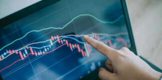 Hand pointing at stock market graph on laptop.