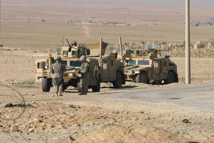 Soldiers beside military vehicles in a desert area.