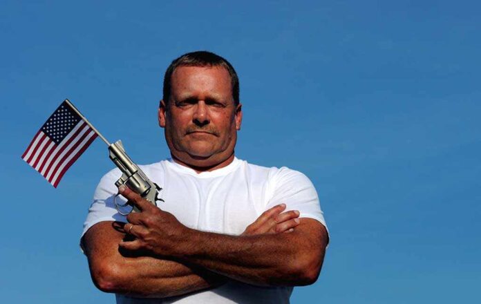 Man holding a gun and an American flag against a blue sky