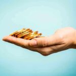 A hand holding a stack of gold coins against a light blue background