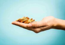 A hand holding a stack of gold coins against a light blue background